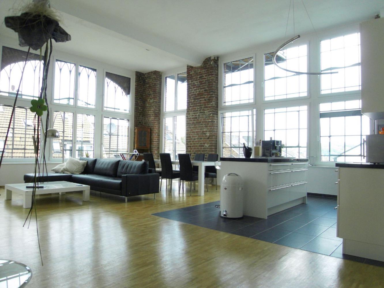 Ein weitläufiger Wohnbereich mit hohen Fenstern, freiliegender Ziegelwand und modernem Interieur.